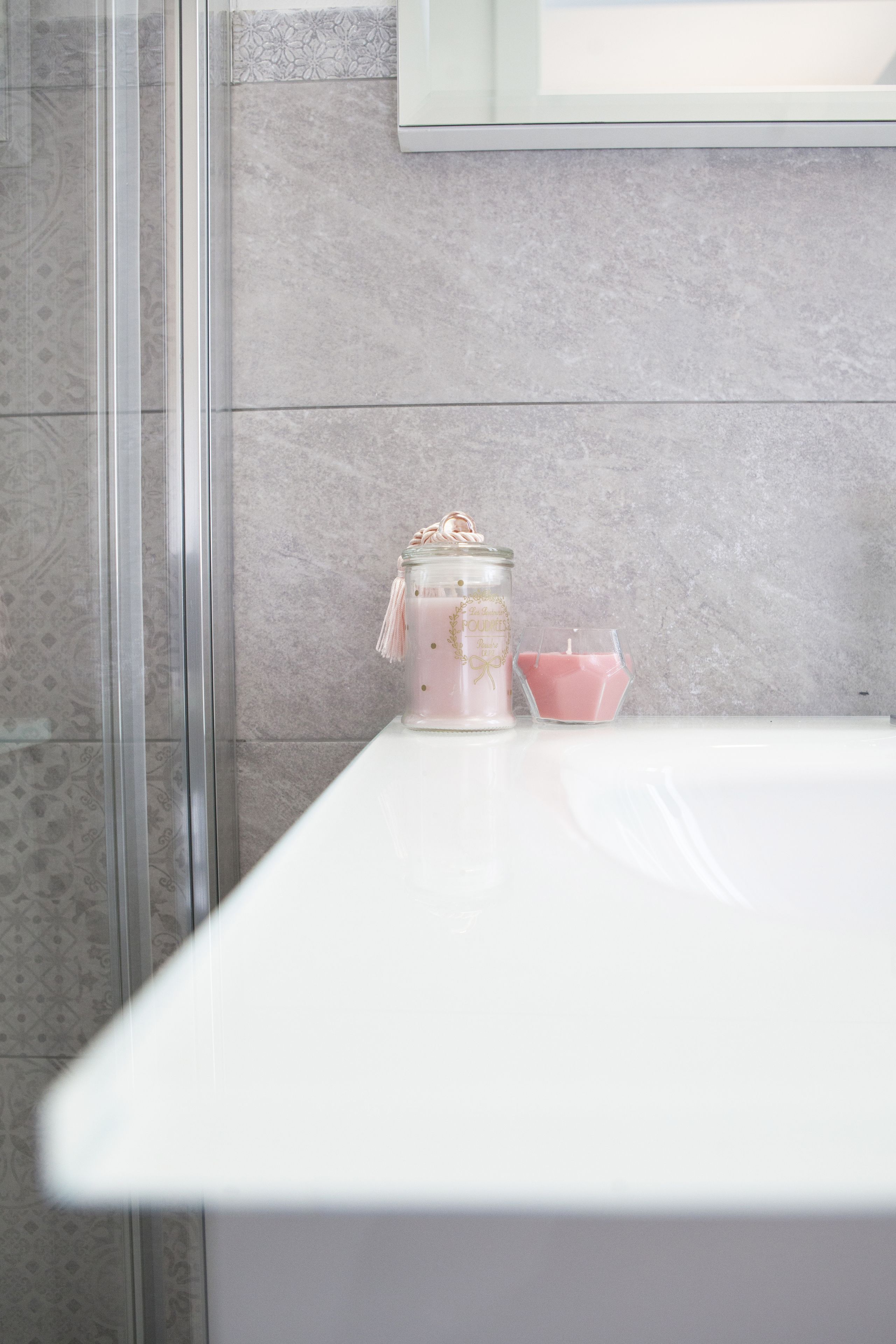 A bathroom with a white bathtub, a glass shower enclosure, and a pink candle on the counter.