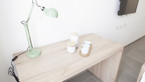 Un escritorio de madera con una lámpara de escritorio verde, un televisor de pantalla plana montado en la pared y una bandeja con tazas y un recipiente.
