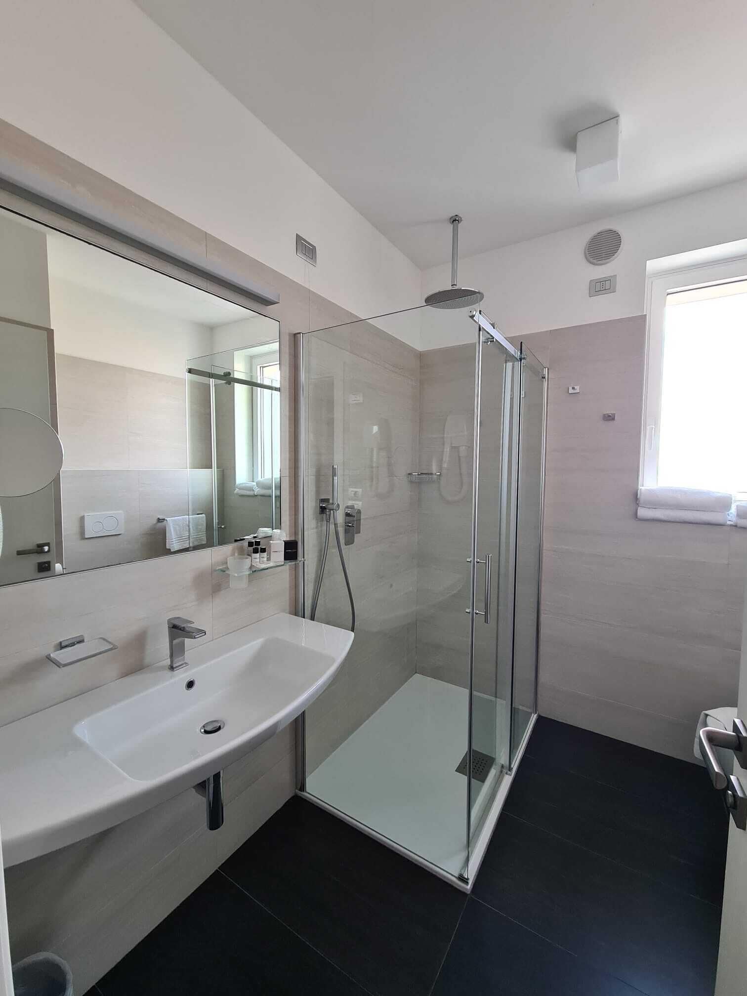 Un baño moderno con ducha de vidrio, lavamanos blanco y un espejo grande.