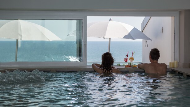 Un couple dans un jacuzzi, avec vue sur la mer grâce à de grandes fenêtres.