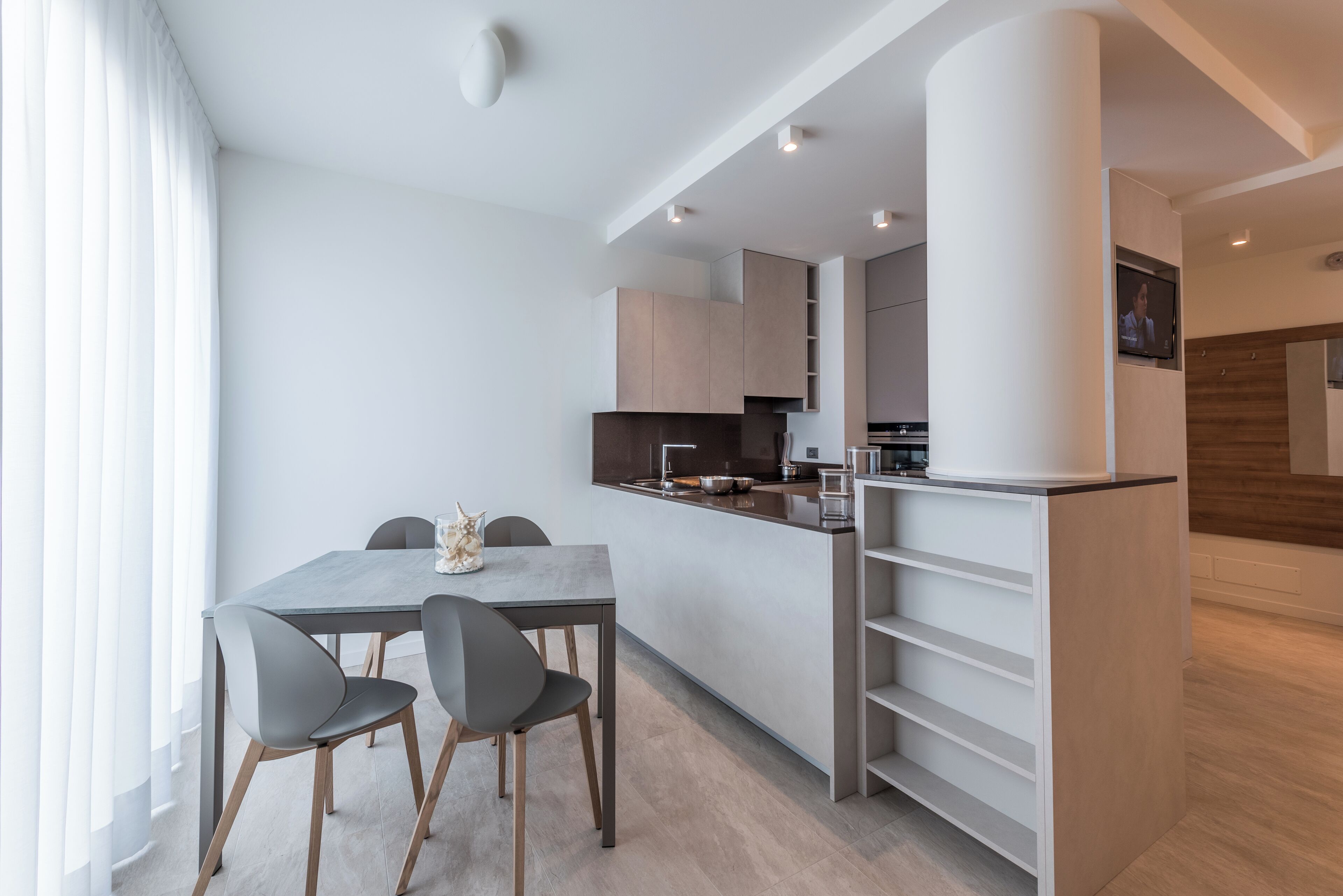 A modern kitchen with a central island, built-in cabinets, and a flat-screen TV mounted on the wall.
