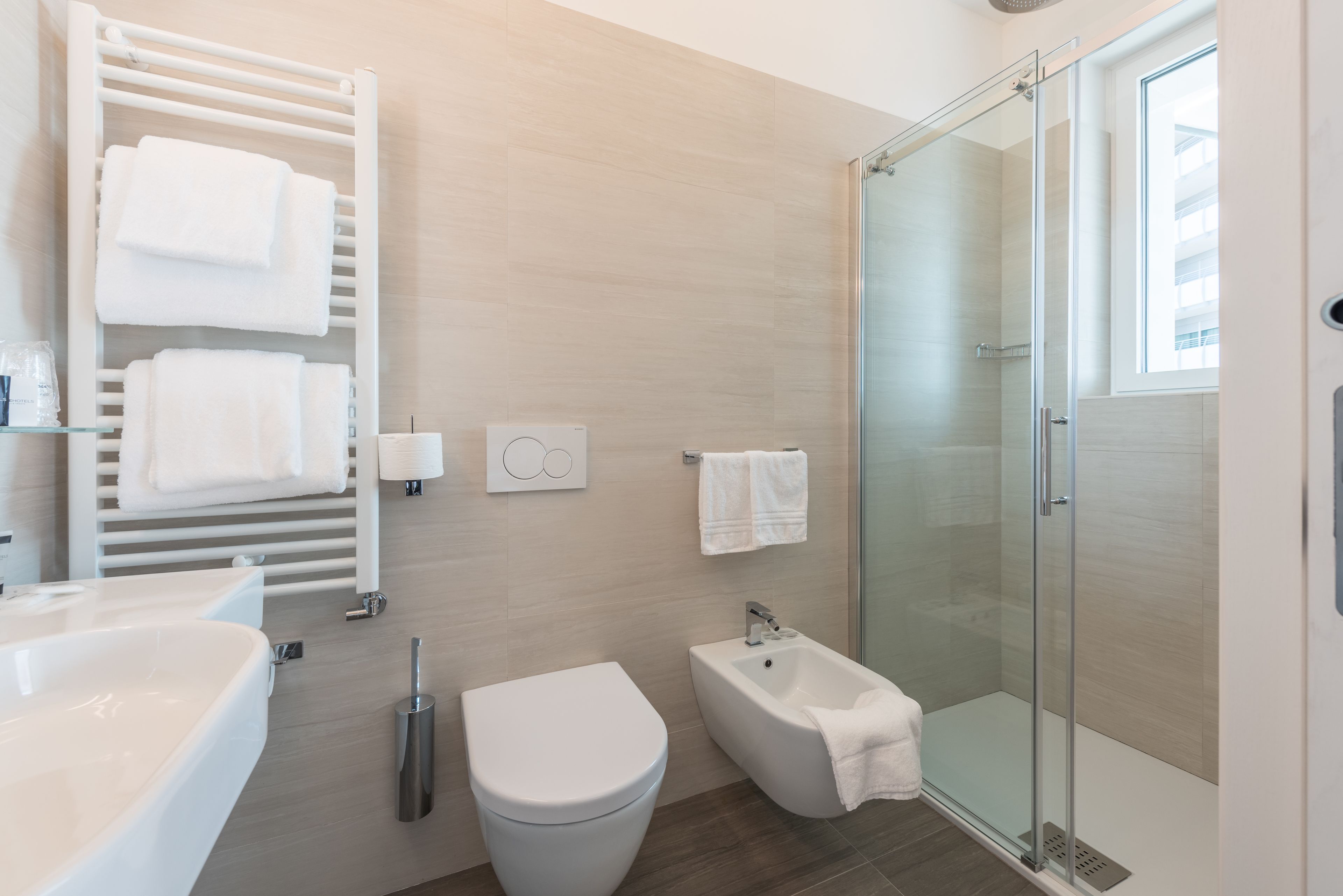Ein modernes Badezimmer mit einer Duschkabine aus Glas, einem weißen Waschbecken, einer Toilette und einem Bidet.
