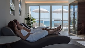 Une salle de spa moderne équipée de deux fauteuils inclinables, d’une petite table et d’une grande fenêtre donnant sur l’océan.