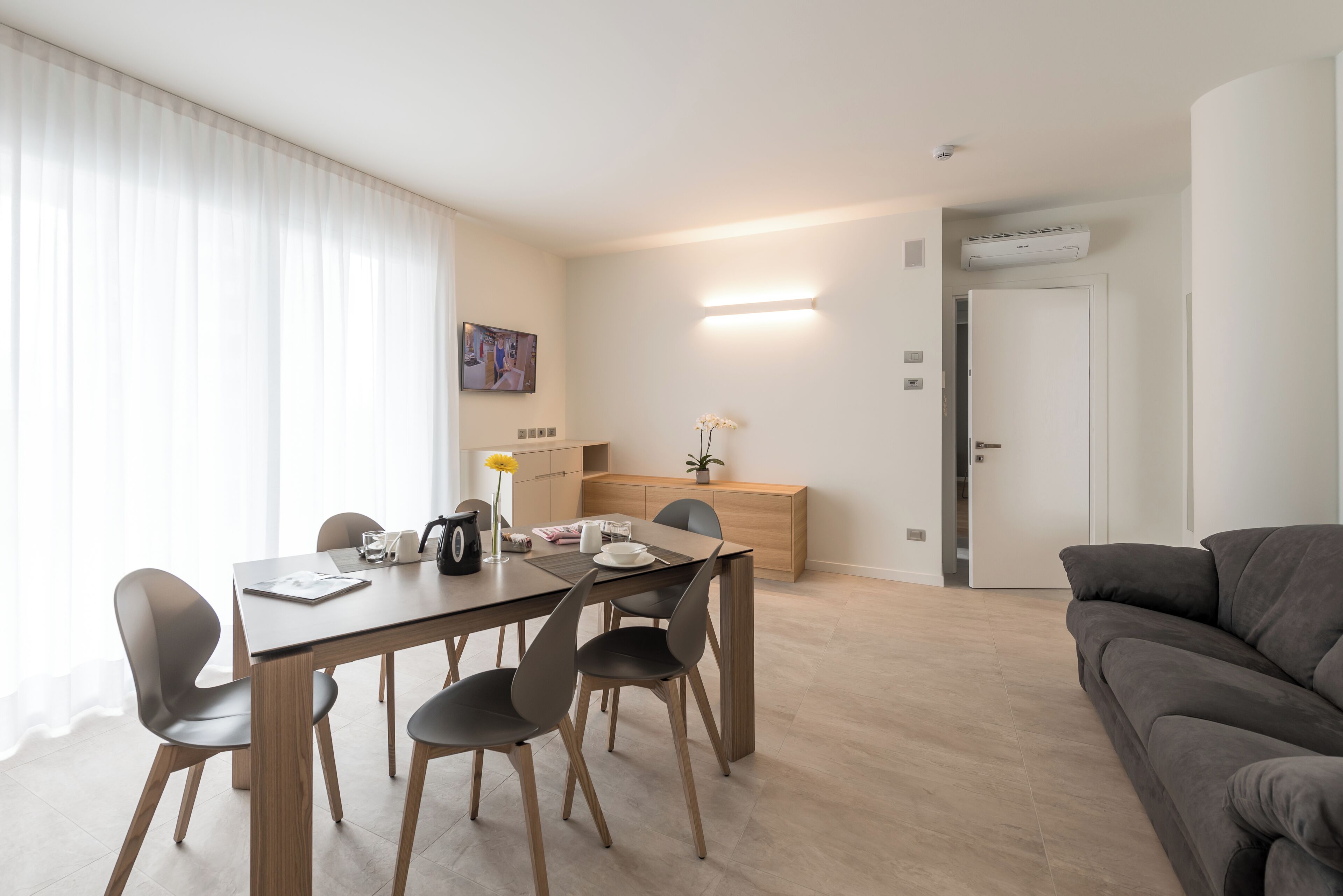 A modern living room with a dining area, a grey sofa, and a wooden dining table with chairs.