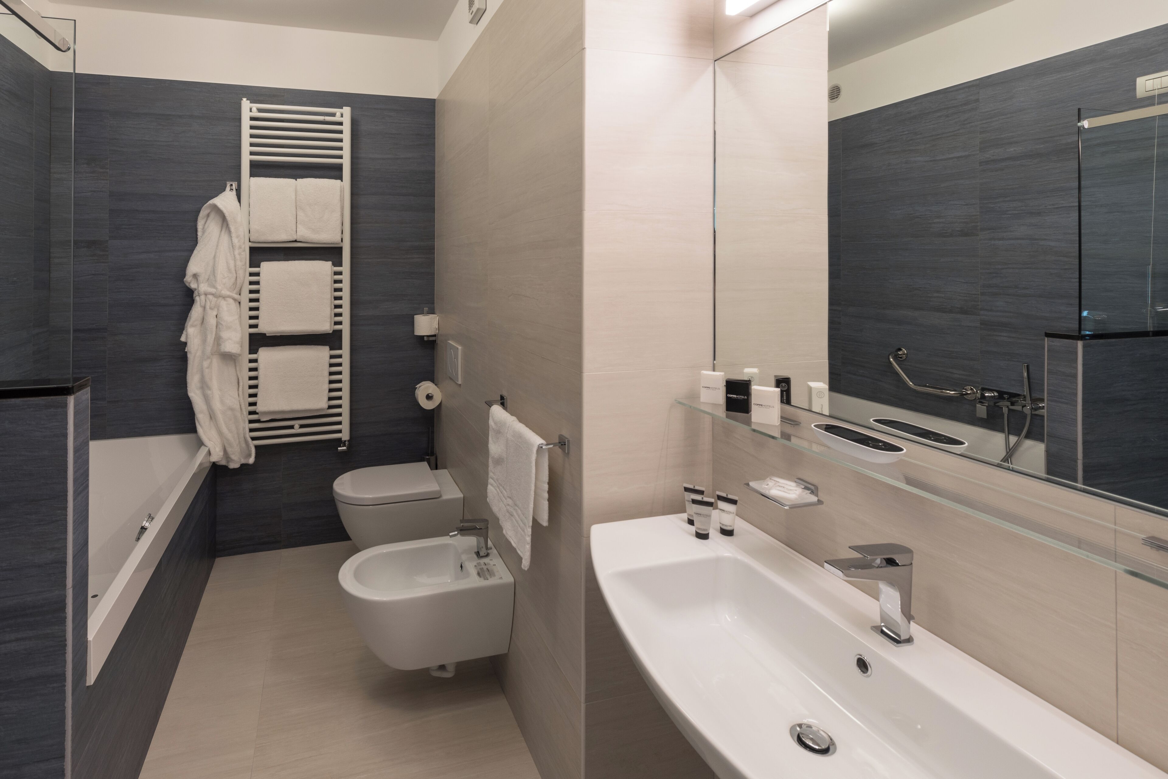 A modern bathroom with a bathtub, toilet, bidet, and a large mirror.