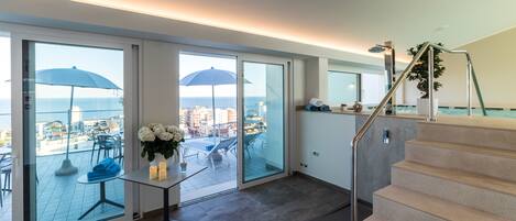 A modern hotel room with a balcony, a staircase, and a view of the sea.