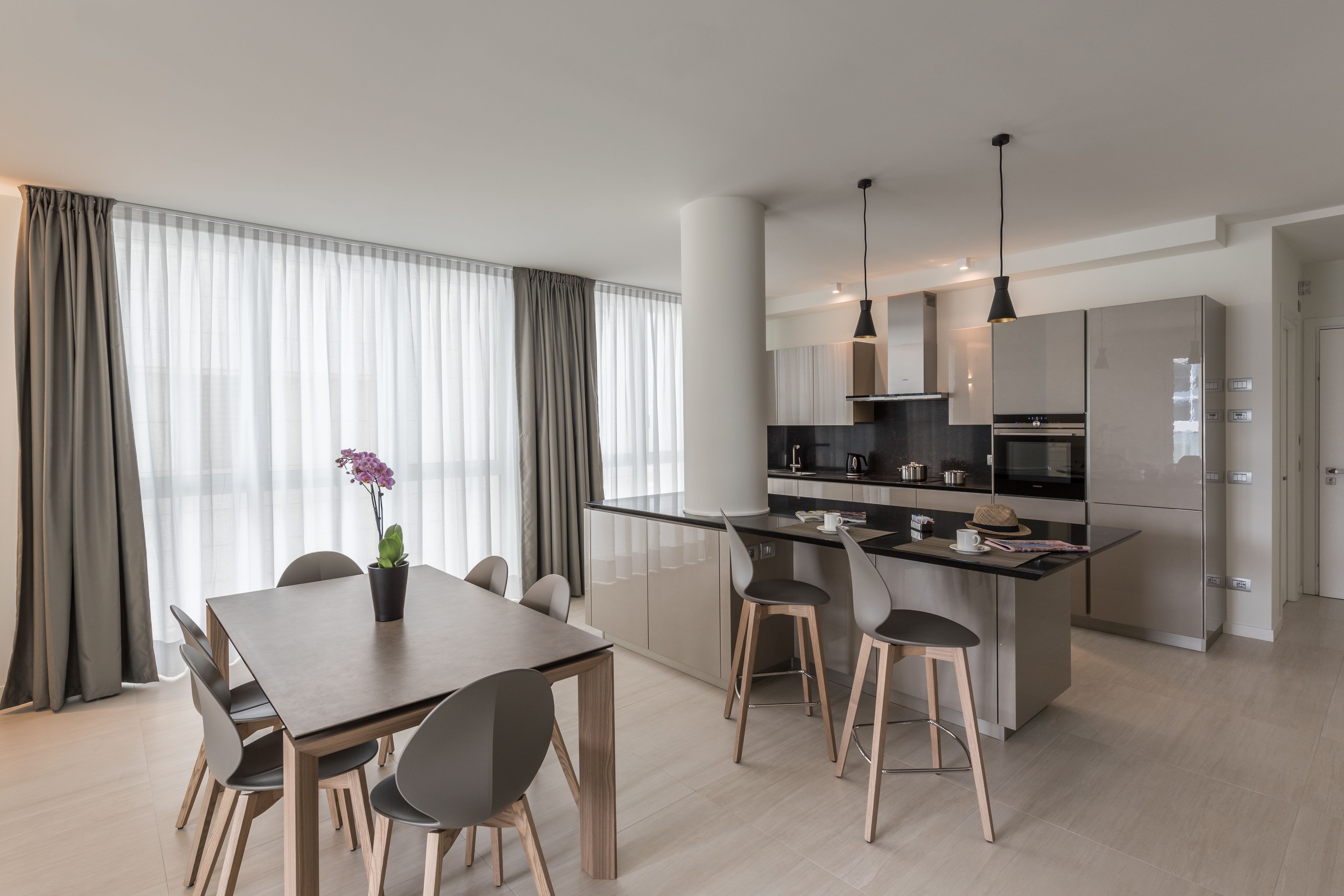 A modern kitchen with a central island, a dining area with a table and chairs, and a large window with curtains.