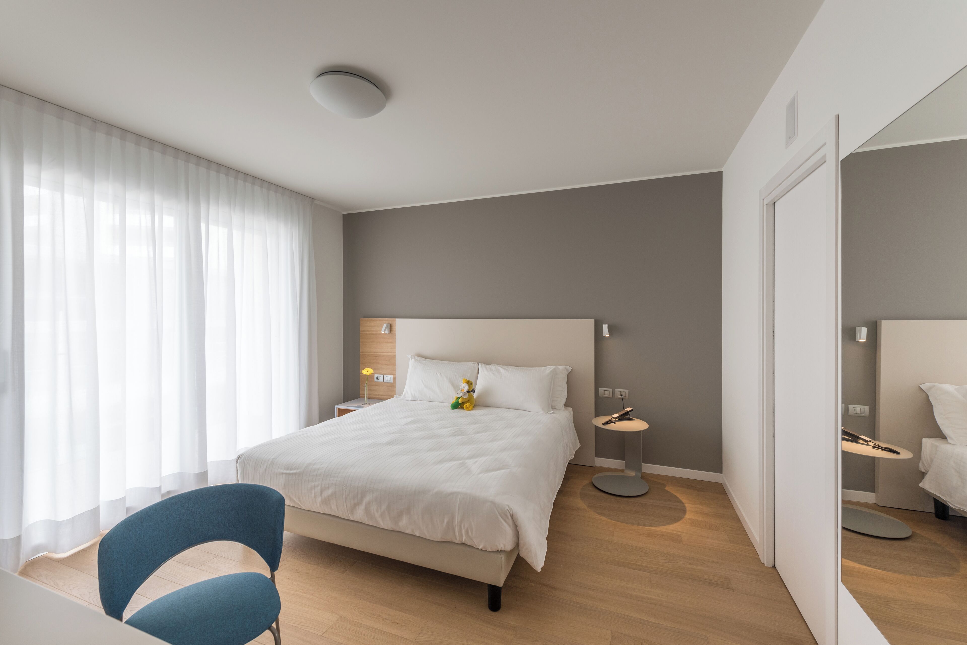 Et moderne hotelværelse med en stor seng, et sengebord, en stol og et spejl.