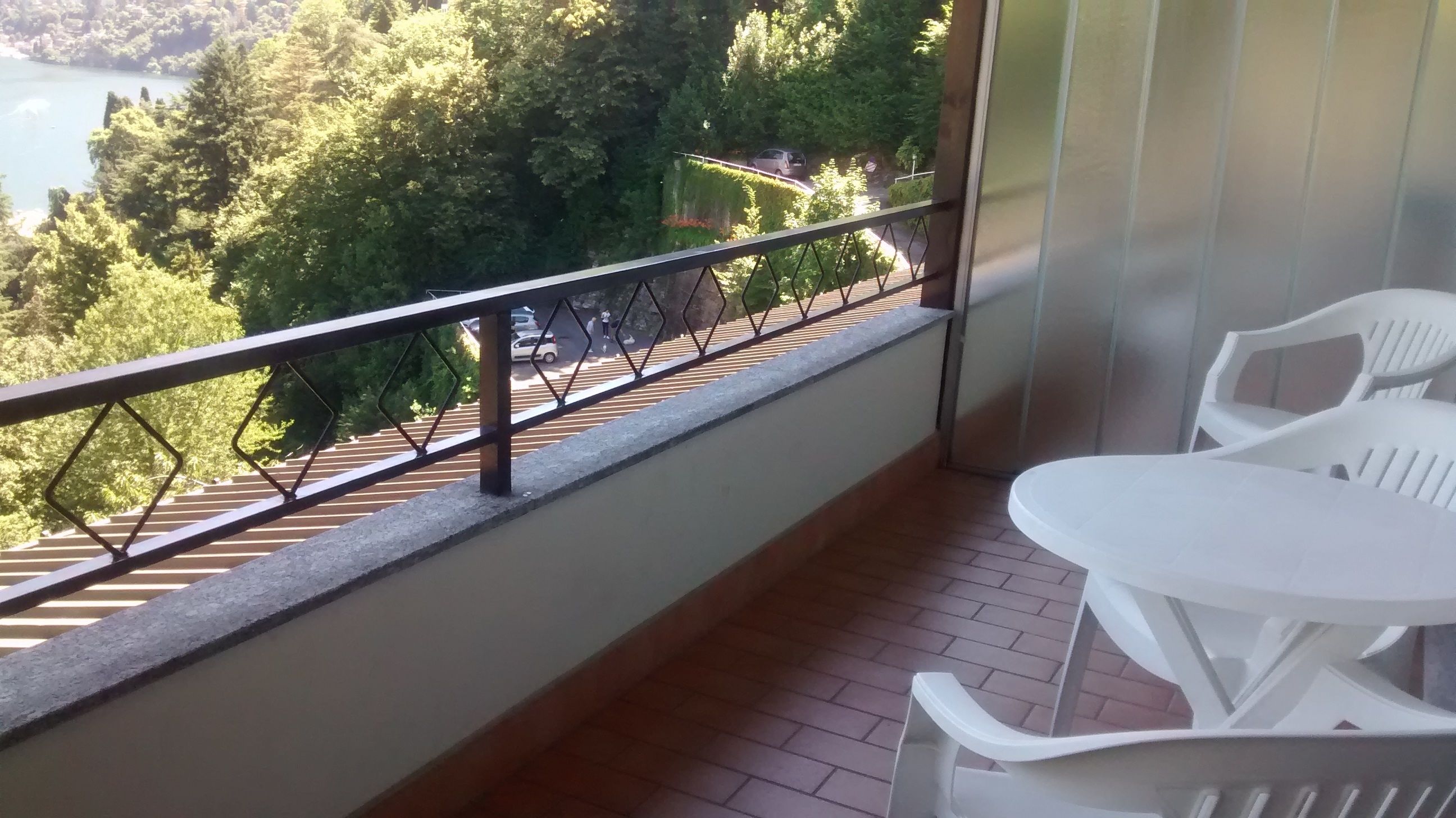 Un balcon doté d’une rambarde en métal, de chaises en plastique blanc et offrant une vue sur un lac et des arbres.