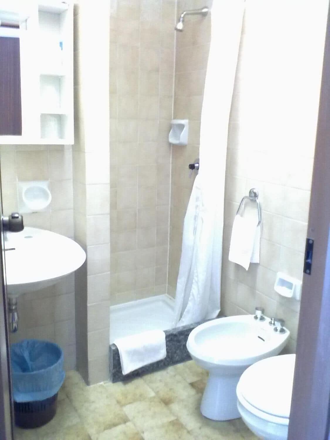 A small bathroom with a sink, toilet, and bidet. There is a shower curtain and a towel rack.