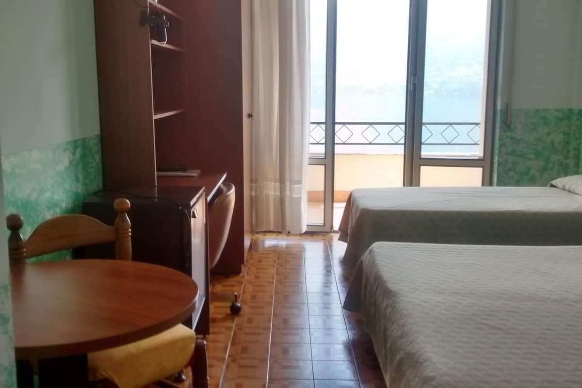 Una camera d'albergo con un letto, una sedia, un tavolino, un armadio e un balcone con vista.