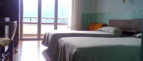 Habitación de hotel con dos camas, un escritorio y una silla. Se ve un balcón desde la ventana grande.