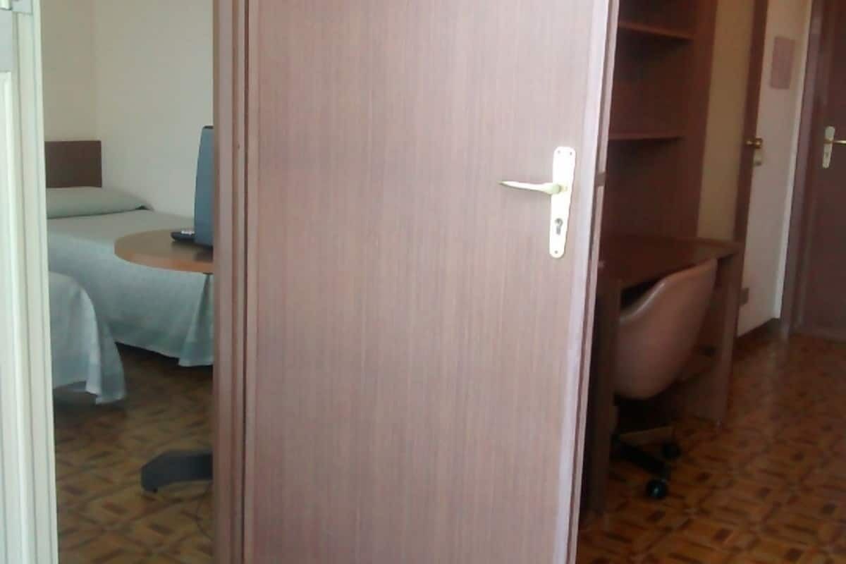 A hotel room with a bed, a small table, a chair, and a bathroom with a toilet and sink.
