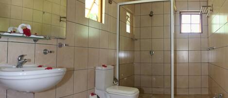 A bathroom with beige tiles, a large mirror, a shower, two toilets, and two sinks.