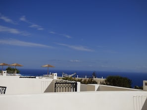 A white building with a black gate, outdoor umbrellas, and a view of the ocean. - Rampelia apartments (Santorini)