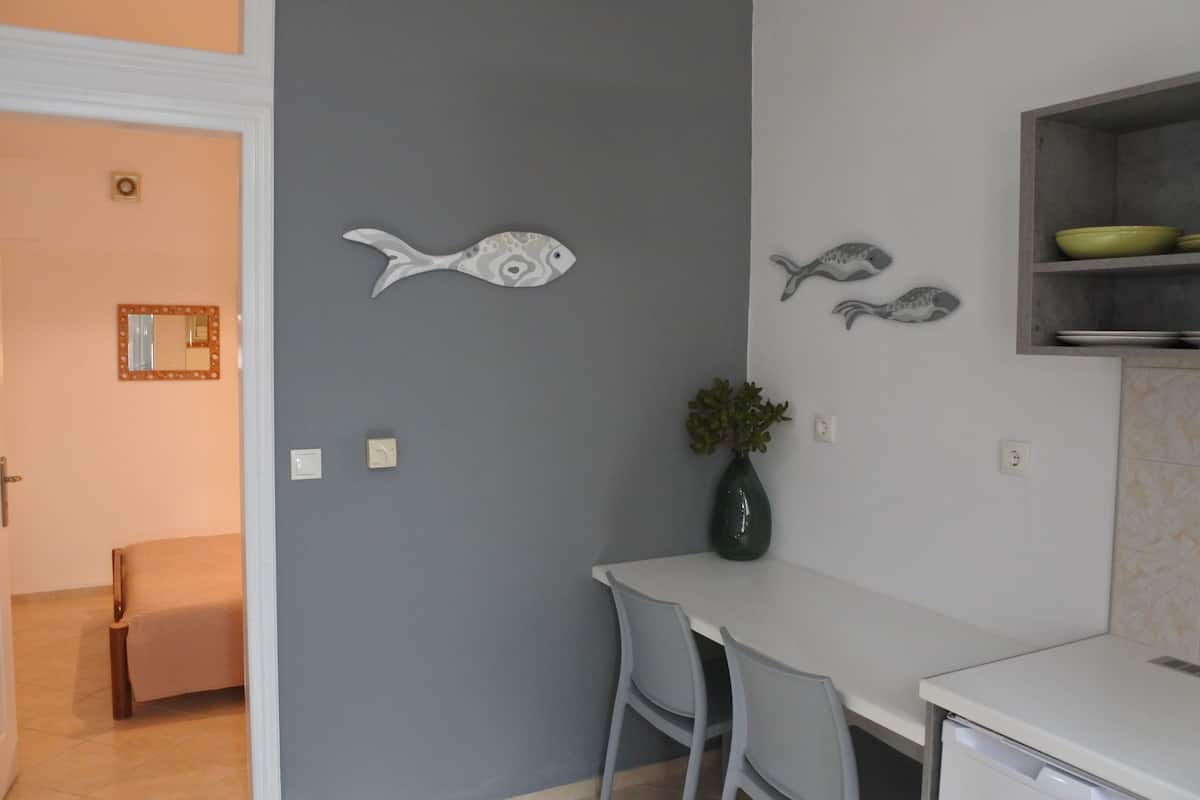 A kitchen with a white countertop, grey wall, and a vase with green plants.