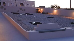 A modern outdoor area with a sloped design, featuring a seating area with steps and a flat surface. - Rampelia apartments (Santorini)
