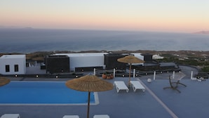 A rooftop pool area with lounge chairs and umbrellas, overlooking a coastal landscape. - Rampelia apartments (Santorini)
