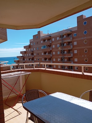 A balcony with a table and chairs, overlooking a building with multiple balconies and a clear view of the sea. - Apartamentos Danesp - Marina D'Or Primera Línea (Oropesa del Mar)