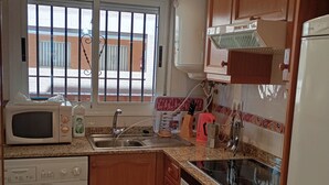 A compact kitchen with a washing machine, microwave, sink, and a refrigerator. - Apartamentos Danesp - Marina D'Or Primera Línea (Oropesa del Mar)