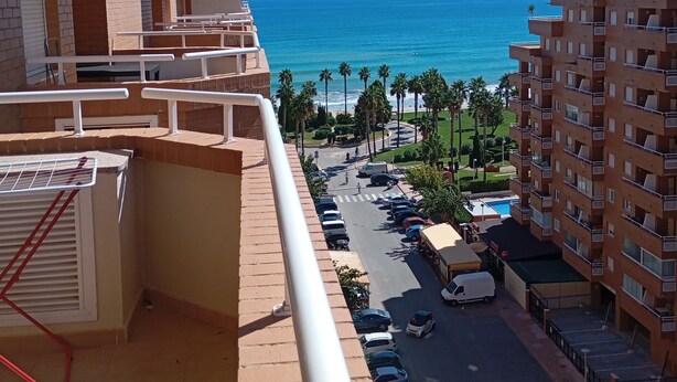 A balcony with a view of the ocean, a parking area, and a multi-story building. - Apartamentos Danesp - Marina D'Or Primera Línea (Oropesa del Mar)