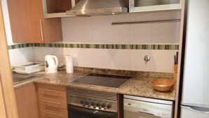 A compact kitchen with a stove, oven, dishwasher, and a microwave above the stove. - Apartamentos Danesp - Marina D'Or Primera Línea (Oropesa del Mar)