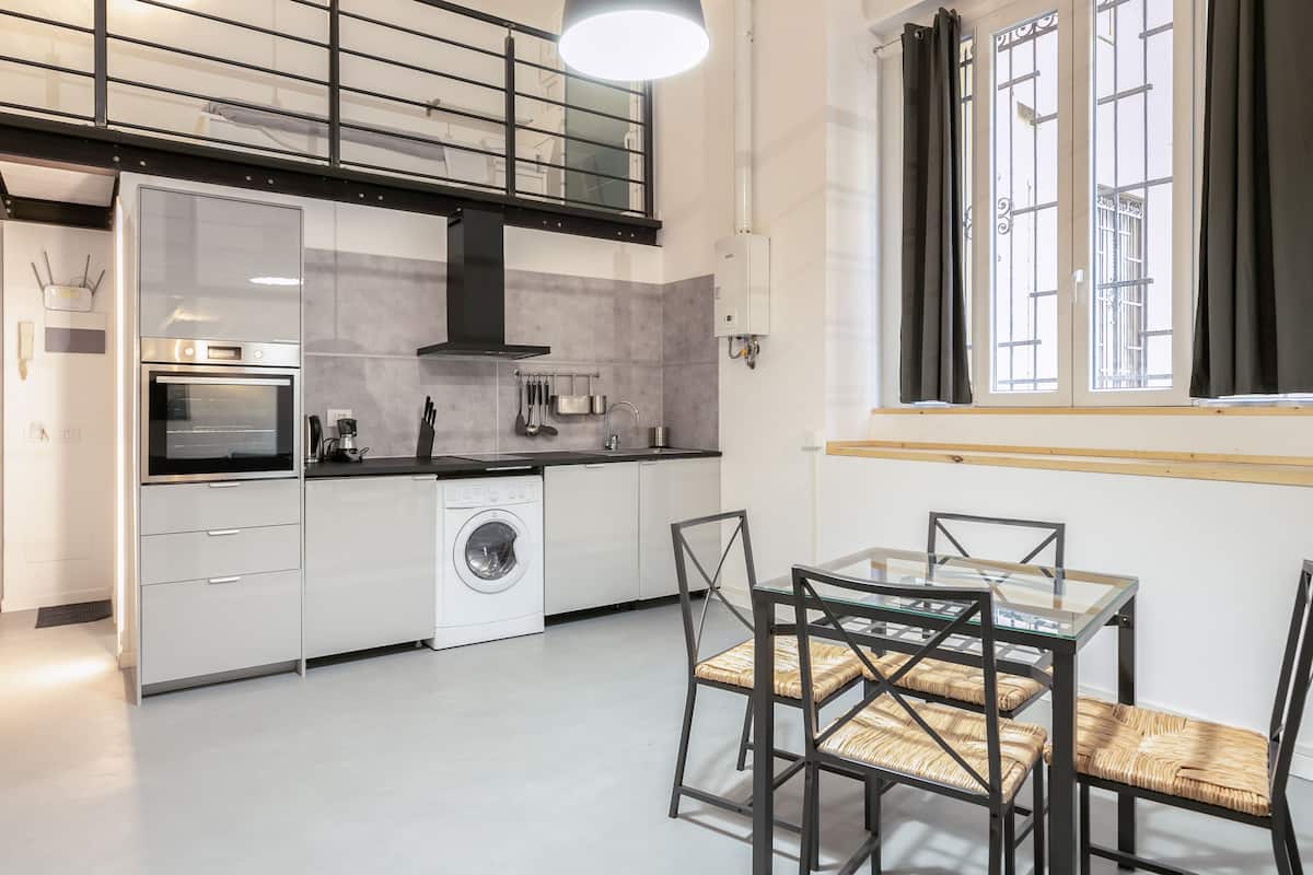 Una cocina moderna con horno empotrado, lavadora y zona de comedor con mesa y sillas de vidrio.