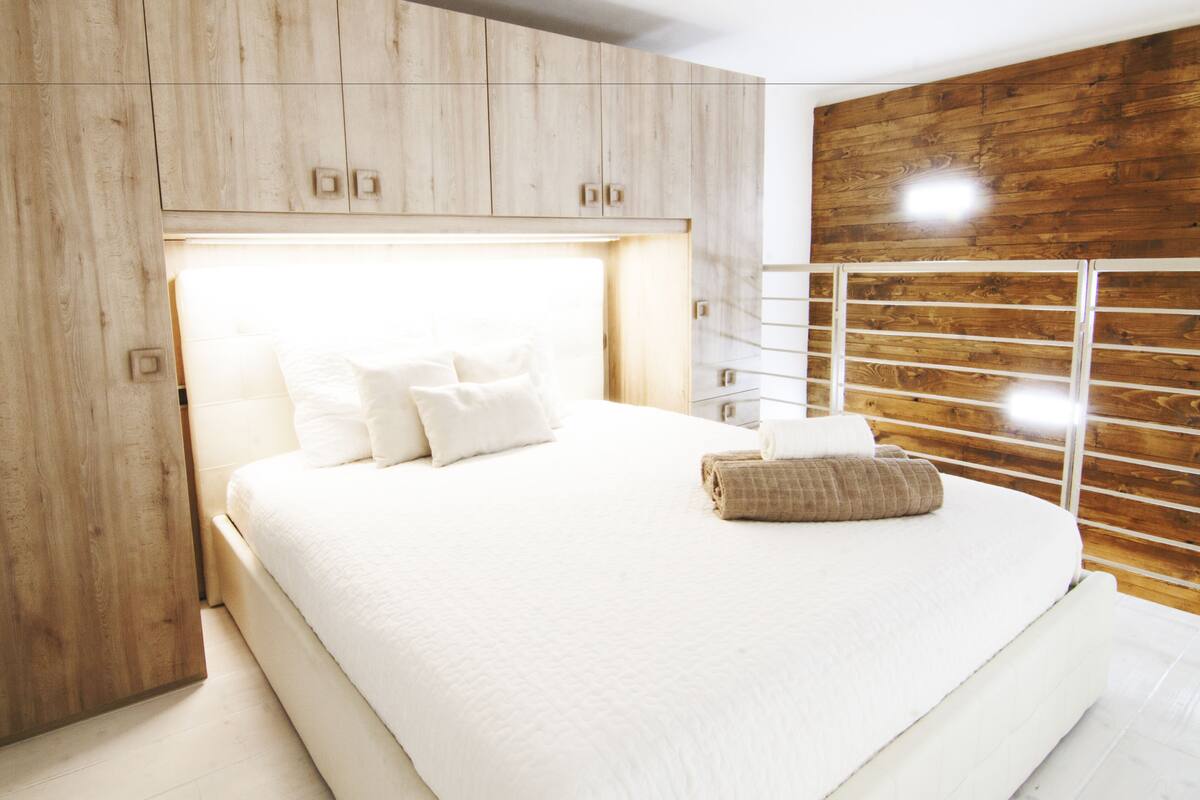 Un dormitorio moderno con una cama grande, paneles de madera y una barandilla de metal.