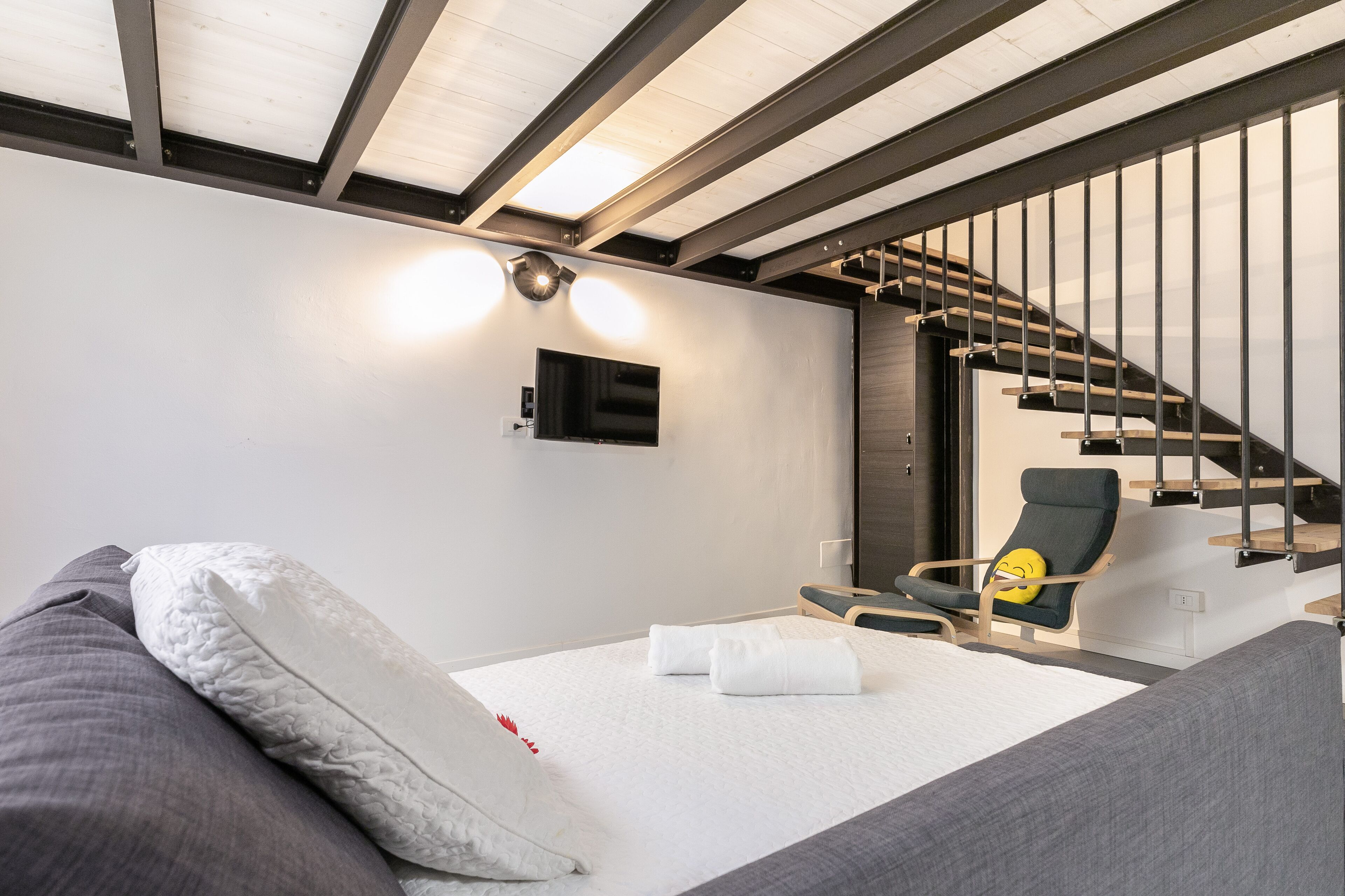 A modern hotel room with a bed, a chair, a TV, and a staircase.