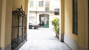 A corridor with a tiled floor, a metal gate, and a building entrance with a green door. - Alessia's Flat - Paolo Sarpi (Milan)