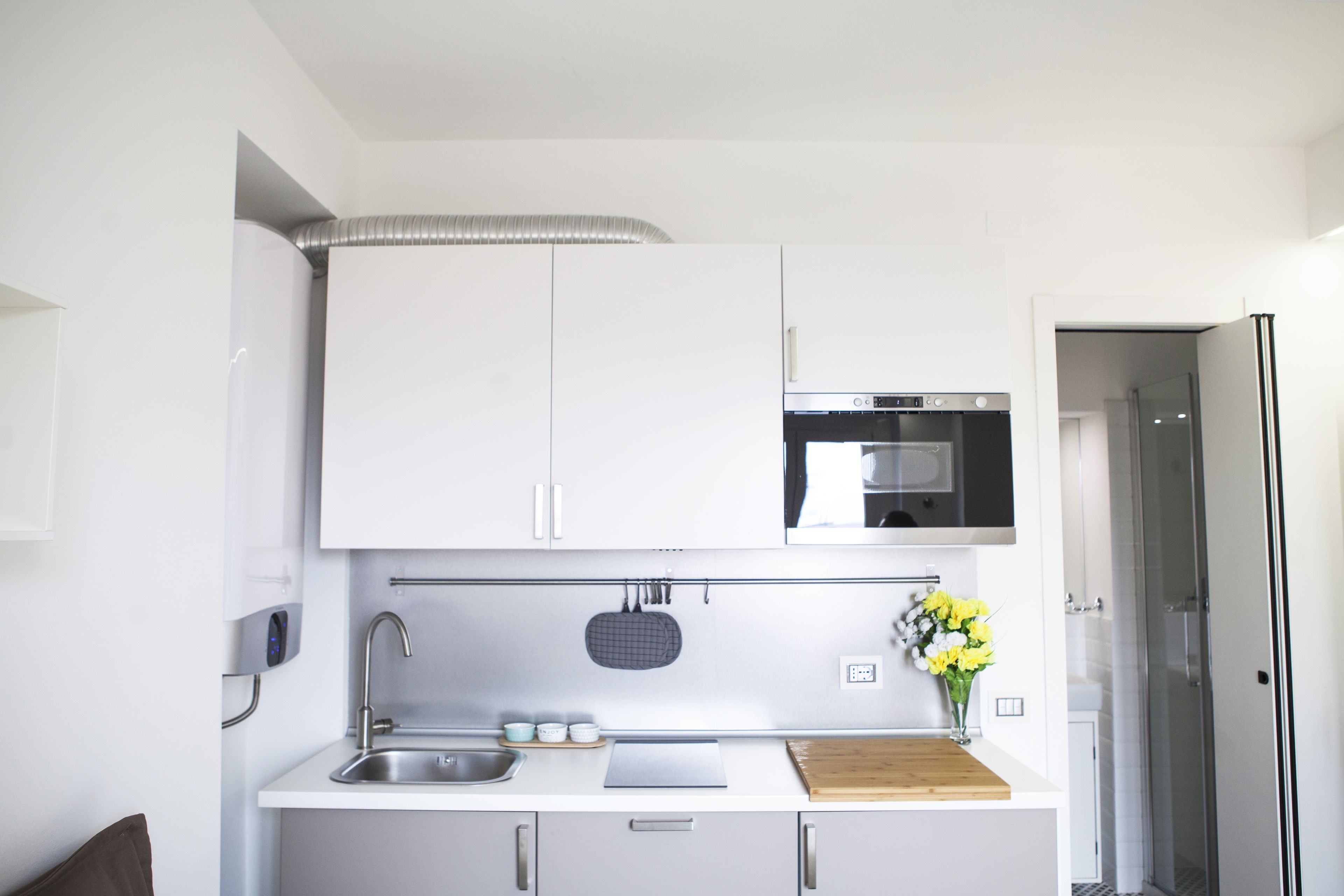 A modern kitchen with white cabinets, a stainless steel sink, a microwave, and a refrigerator.