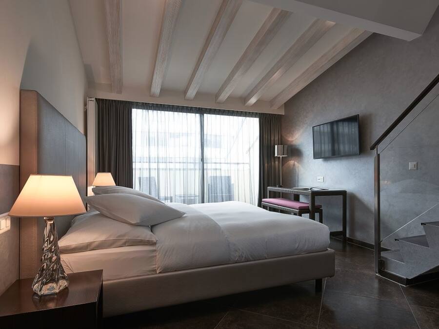 Una habitación de hotel moderna con una cama grande, un escritorio con lámpara, un televisor montado en la pared y una escalera.