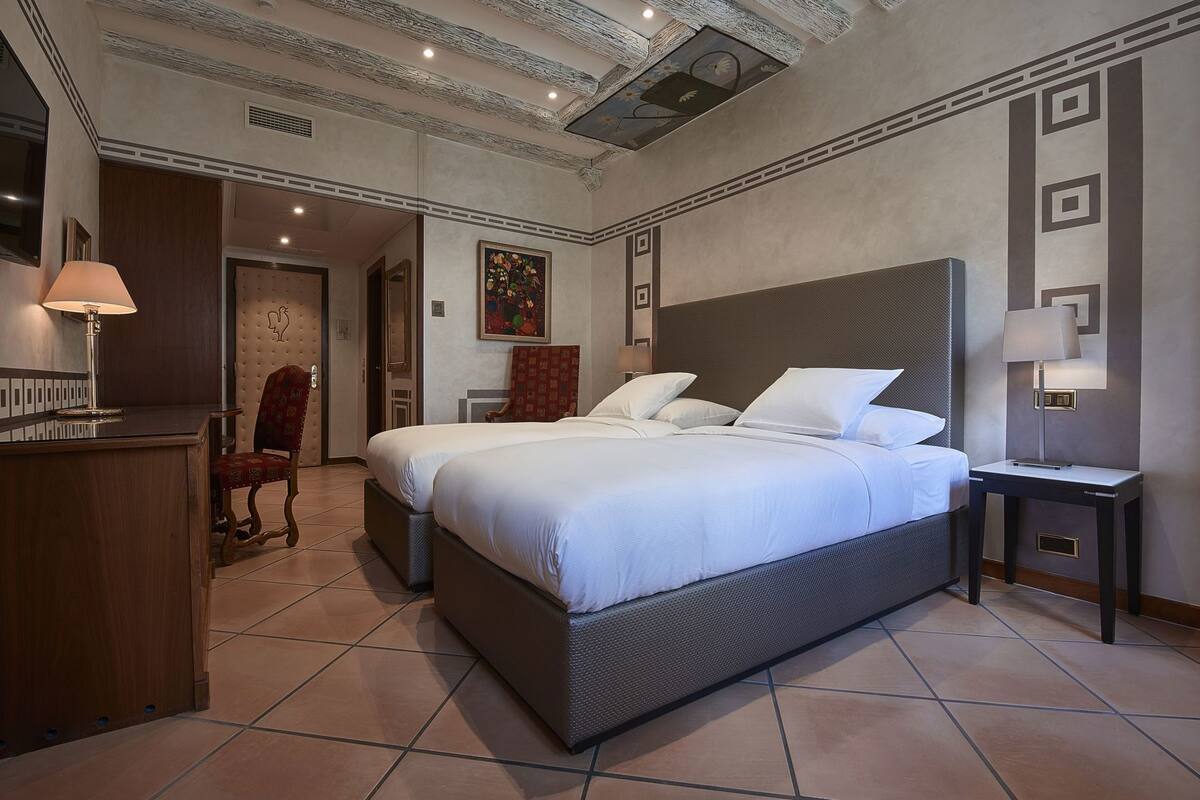A hotel room with a large bed, two bedside tables, a desk, a chair, and a door leading to another room.
