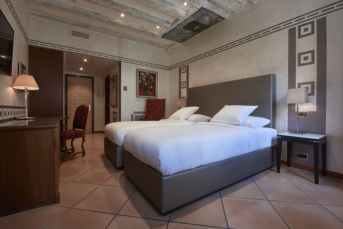 A hotel room with a large bed, a desk, a chair, and a small table with a lamp.