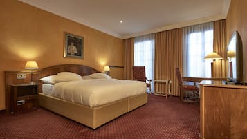 A hotel room with a large bed, two bedside tables with lamps, a wooden desk, a chair, and a large mirror.