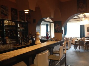 Zona de bar con una barra larga, estantes con botellas y sillas.