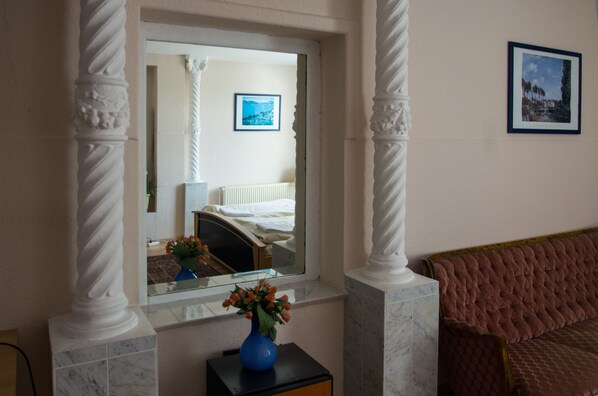 Una habitación con una cama, una ventana con vistas, un florero con flores y un cuadro en la pared.