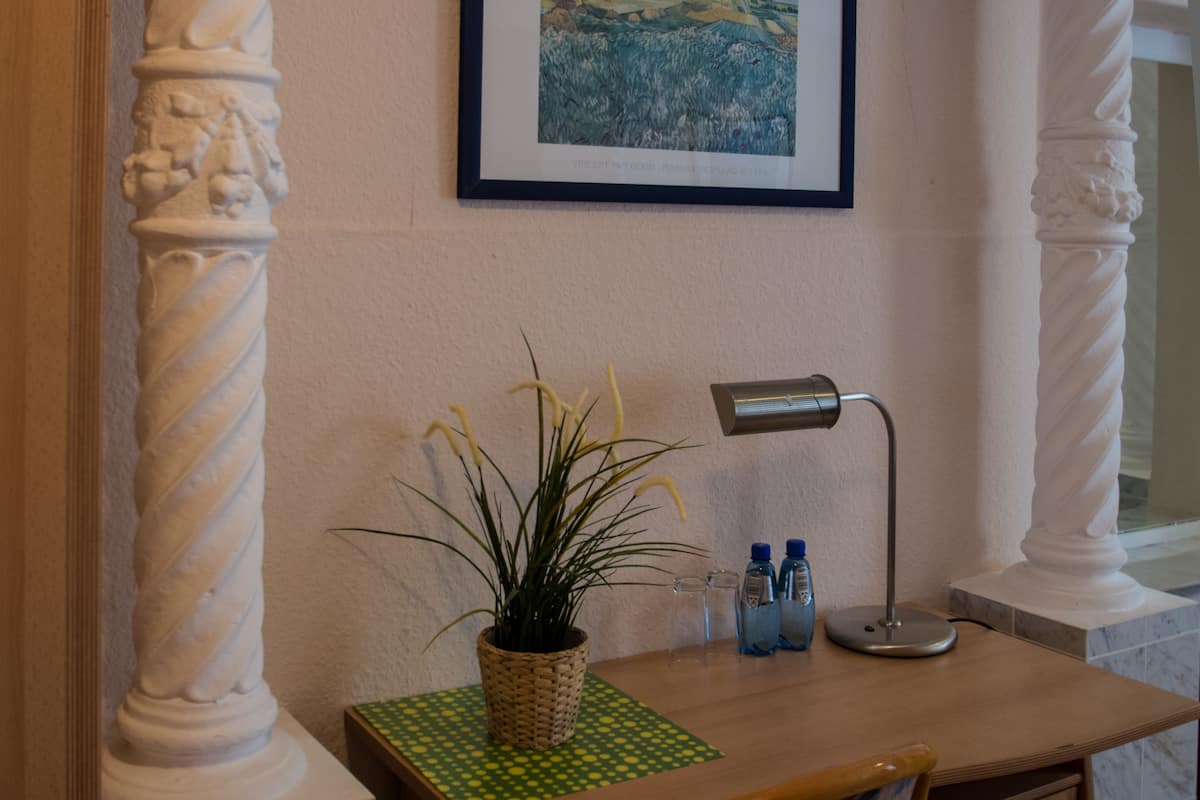 Ein Zimmer mit einem Holztisch, einer Topfpflanze, einer Lampe und einem gerahmten Bild an der Wand.
