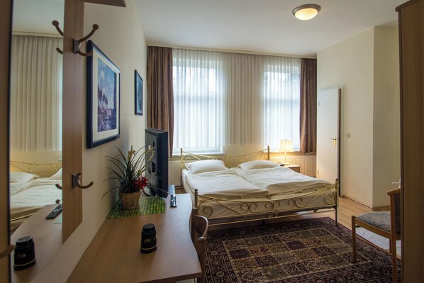 Habitación de hotel con cama, escritorio con silla, taza de café, planta y ventana con cortinas.