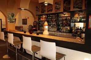 A bar area with white bar stools, a counter with various bottles and glasses, and a decorative white vase. - Hotel Apex (Hemmingen)