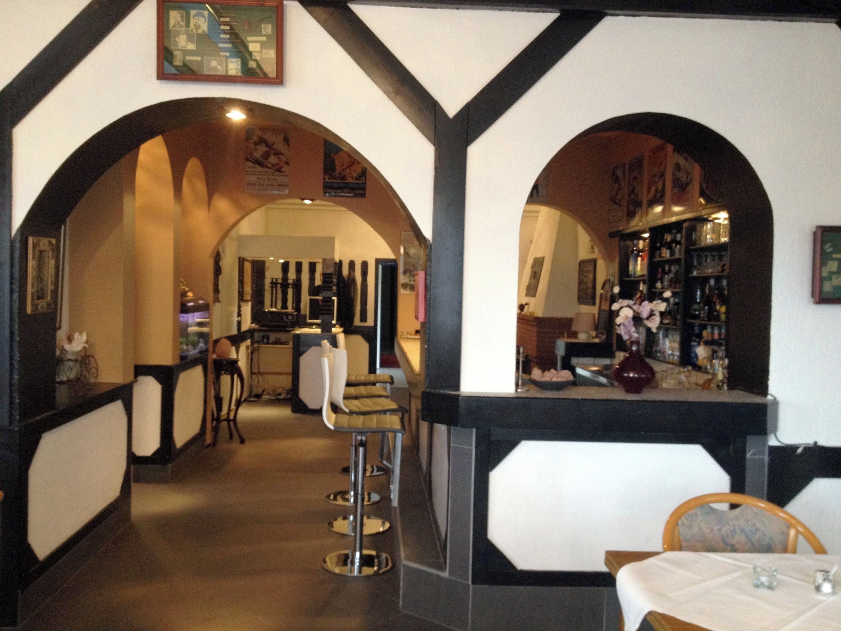 Interior de un restaurante con barra, sillas altas y mostrador exhibiendo botellas.
