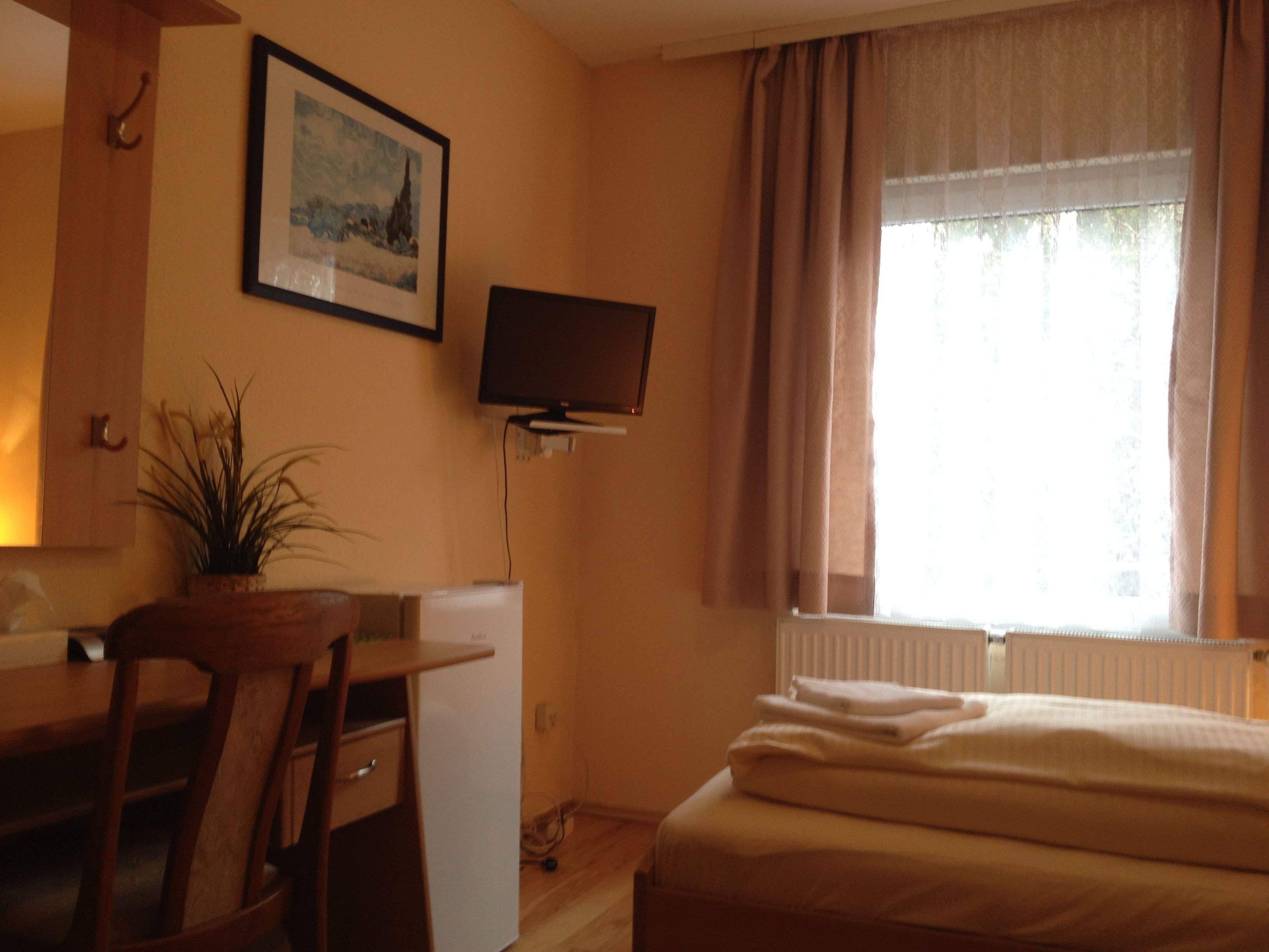 Una habitación de hotel con cama, escritorio y silla, televisor montado en la pared y ventana con cortinas.