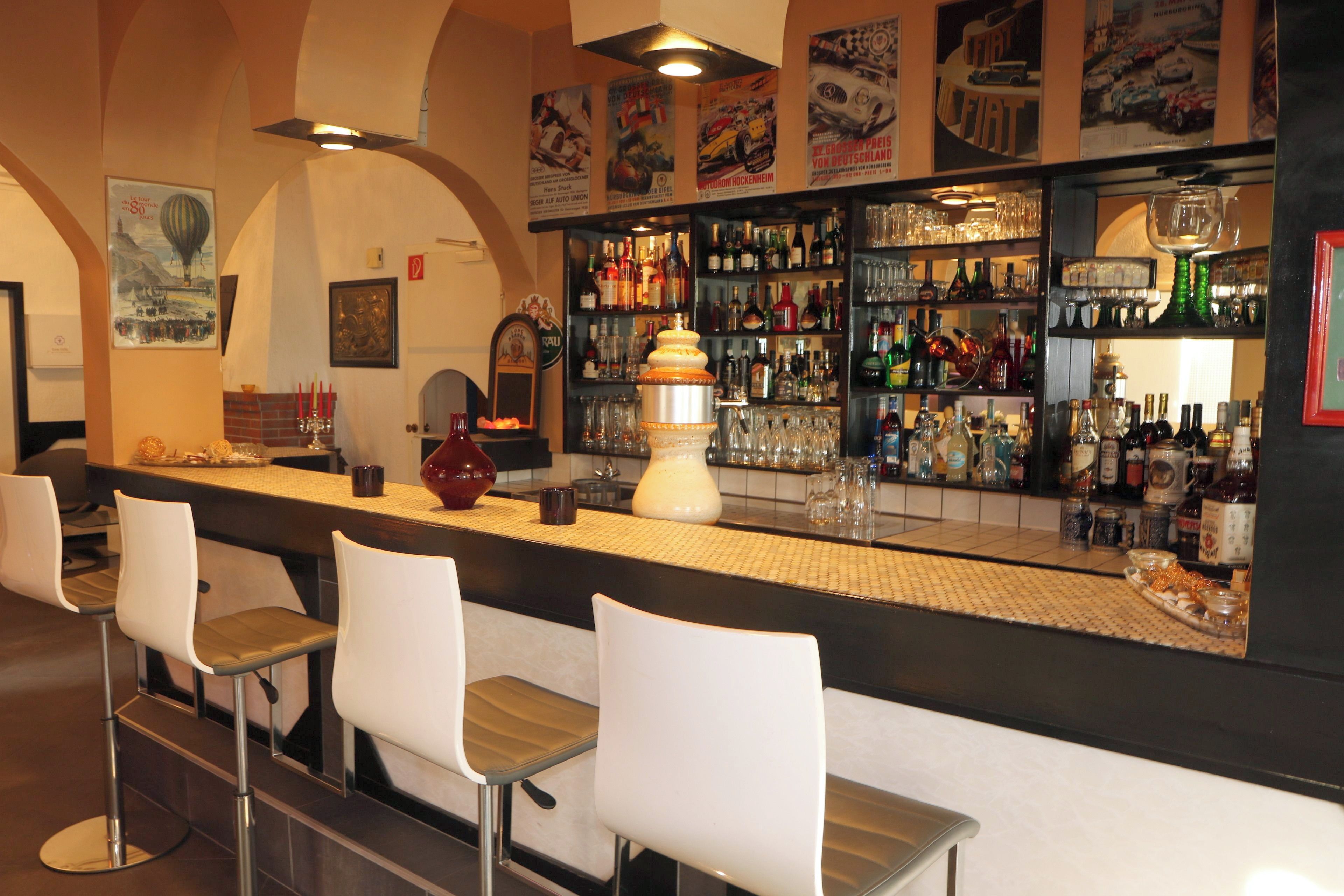 Zona de bar con mostrador, taburetes y una variedad de botellas y vasos.