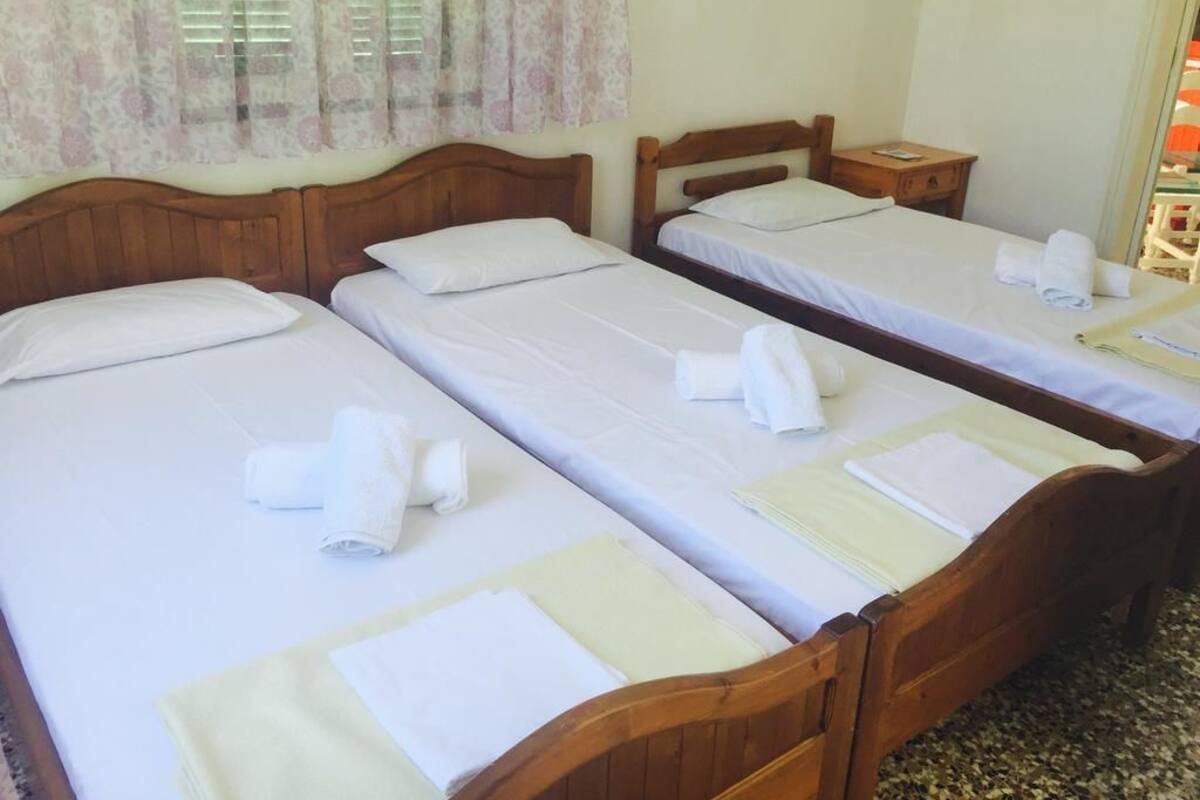 A hotel room with three wooden beds, each with white linens and towels.