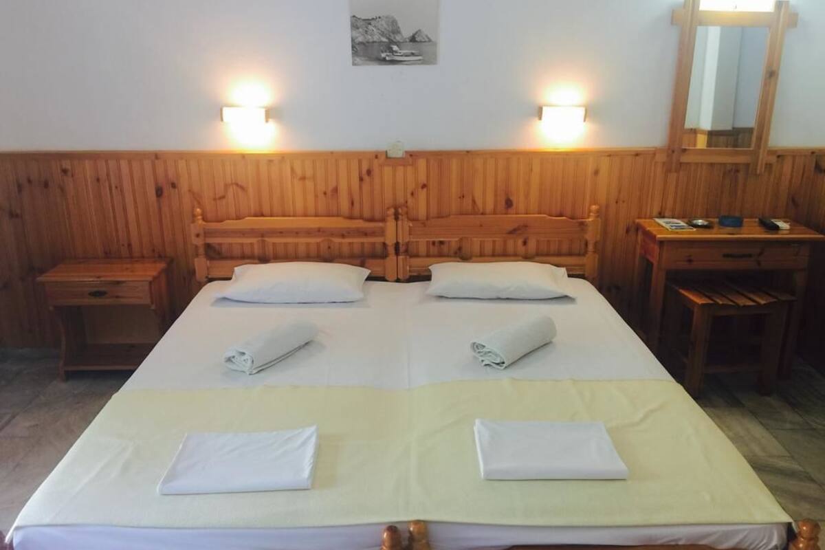 A hotel room with two beds, wooden headboard, bedside lamps, a desk, and a mirror.