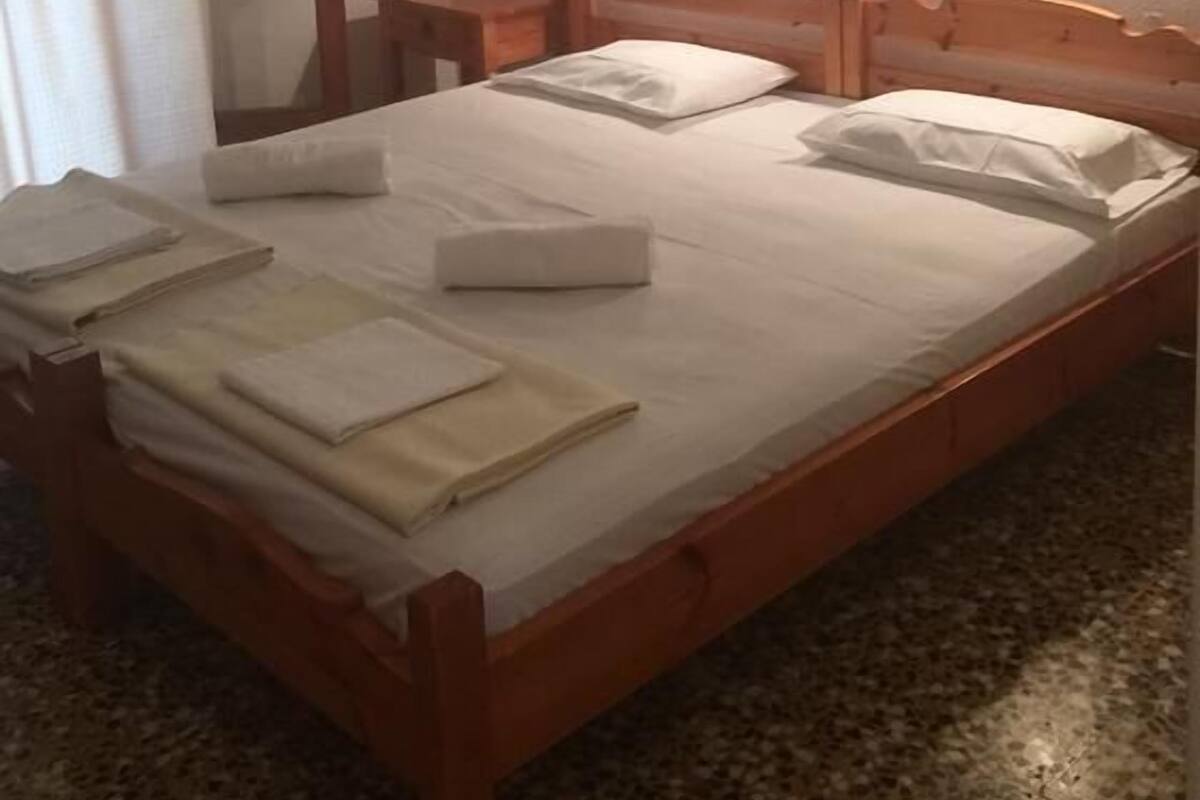 A neatly made bed with pillows and folded towels, a wooden headboard, two bedside tables with lamps, a mirror, and a framed picture on the wall.
