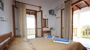 Una habitación de hotel con una cama, un banco de madera, una mesita, un espejo y un balcón con barandilla.