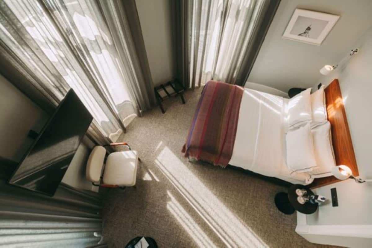 A hotel room with a bed, a TV, a chair, and a small table with a lamp.