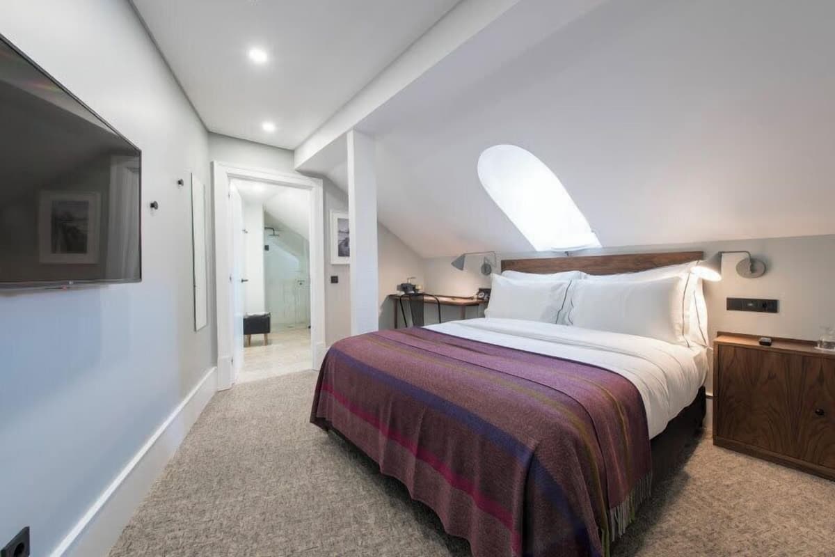 A bedroom with a bed, a nightstand, a wooden cabinet, a ceiling light, and a door leading to another room.