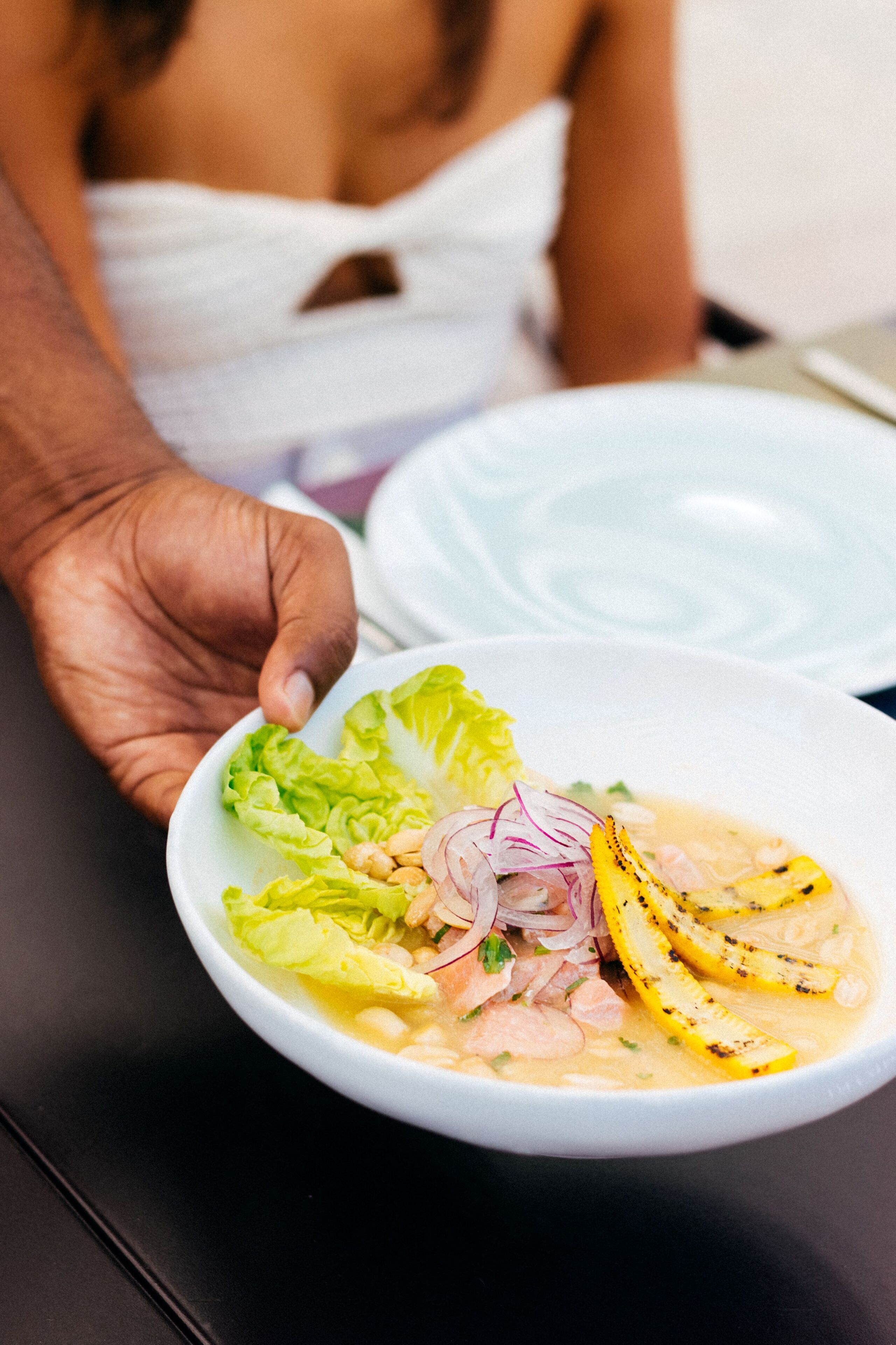 A bowl of soup with vegetables and a plate of food.